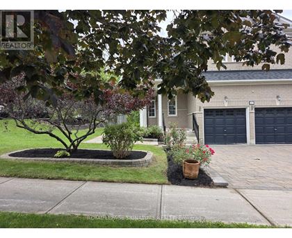 A tree in a flower bed in front of a house with a Royal LePage sign.