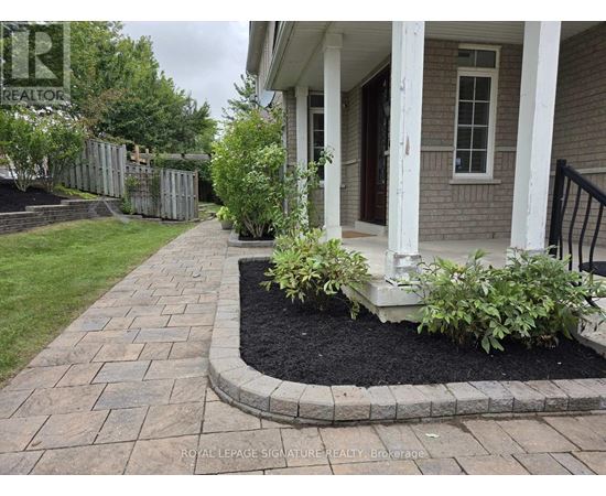 A brick walkway leads to a house with a white porch.