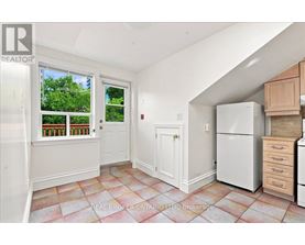 A kitchen with a refrigerator, cabinets, and a window with a view of trees.