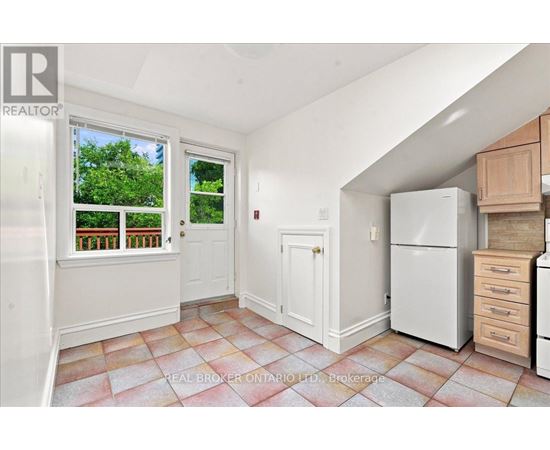 A kitchen with a refrigerator, cabinets, and a window with a view of trees.