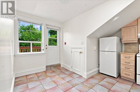 A kitchen with a refrigerator, cabinets, and a window with a view of trees.