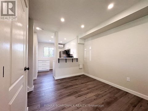 A spacious room with wooden floors and white walls, featuring a flat-screen TV and a built-in cabinet.