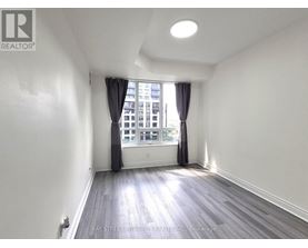 A spacious room with wooden flooring and a window with curtains.