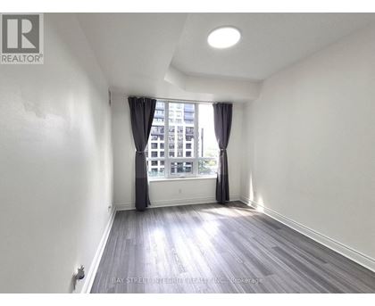 A spacious room with wooden flooring and a window with curtains.