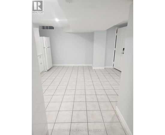 A white tiled kitchen with a refrigerator and a door on the right.