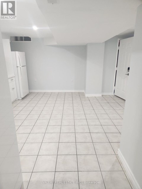 A white tiled kitchen with a refrigerator and a door on the right.