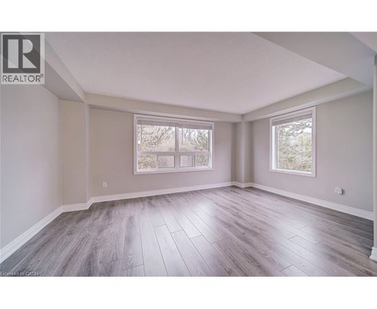 A spacious room with wood flooring and two windows.
