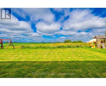 A grassy field with a swing set and a small house in the distance.