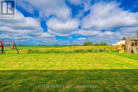 A grassy field with a swing set and a small house in the distance.