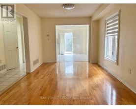 A spacious room with wooden floors and a view of a green outdoor area through a sliding glass door.