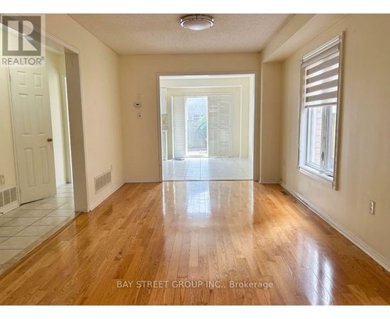 A spacious room with wooden floors and a view of a green outdoor area through a sliding glass door.