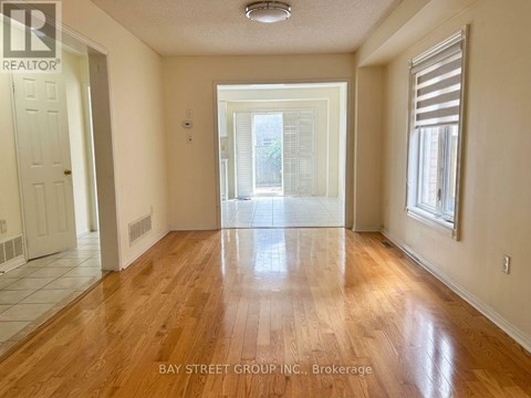 A spacious room with wooden floors and a view of a green outdoor area through a sliding glass door.