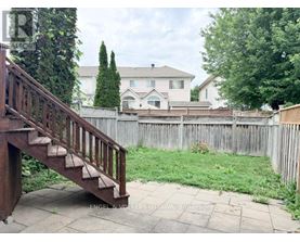 A wooden staircase leads to a house with a white fence and green trees in the background.