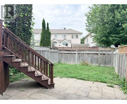 A wooden staircase leads to a house with a white fence and green trees in the background.