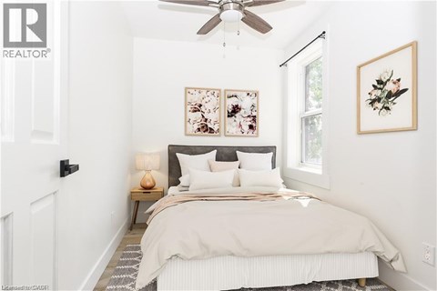 A bedroom with a bed, a ceiling fan, and two framed pictures on the wall.