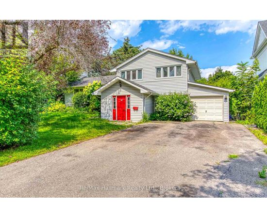 A house with a red door is surrounded by greenery and has a driveway leading to the garage.