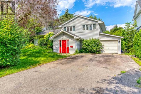 A house with a red door is surrounded by greenery and has a driveway leading to the garage.