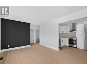 A spacious, empty room with a kitchen area visible through the open door.