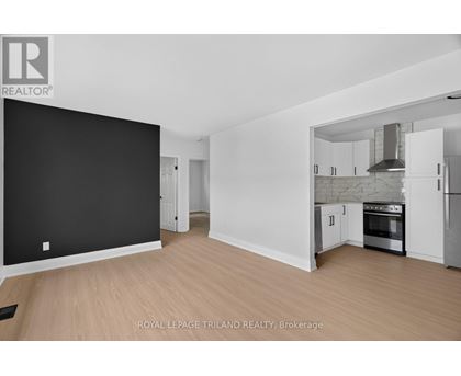 A spacious, empty room with a kitchen area visible through the open door.