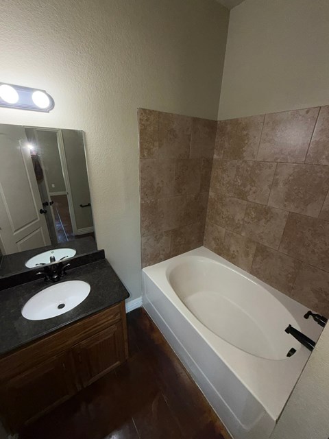A bathroom with a white bathtub, black countertop, and brown tiles.