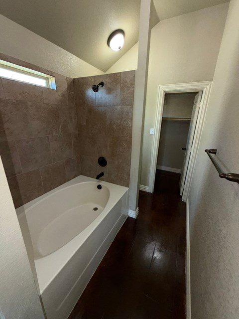 A bathroom with a white bathtub and brown tiled walls.