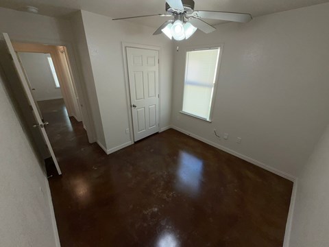 A room with a brown floor and a ceiling fan.
