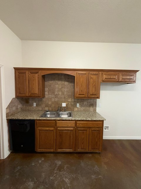A kitchen with brown cabinets and a black dishwasher.