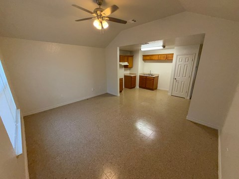 A room with a ceiling fan and a kitchenette in the background.