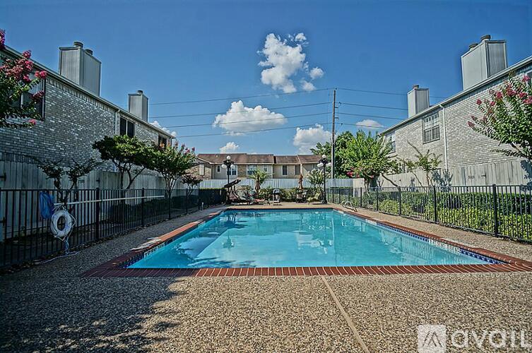 A pool surrounded by a brick border with a fence and houses in the background.