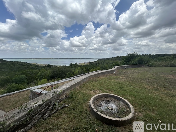 A fountain in the middle of a grassy area with a wooden walkway leading to the ocean.