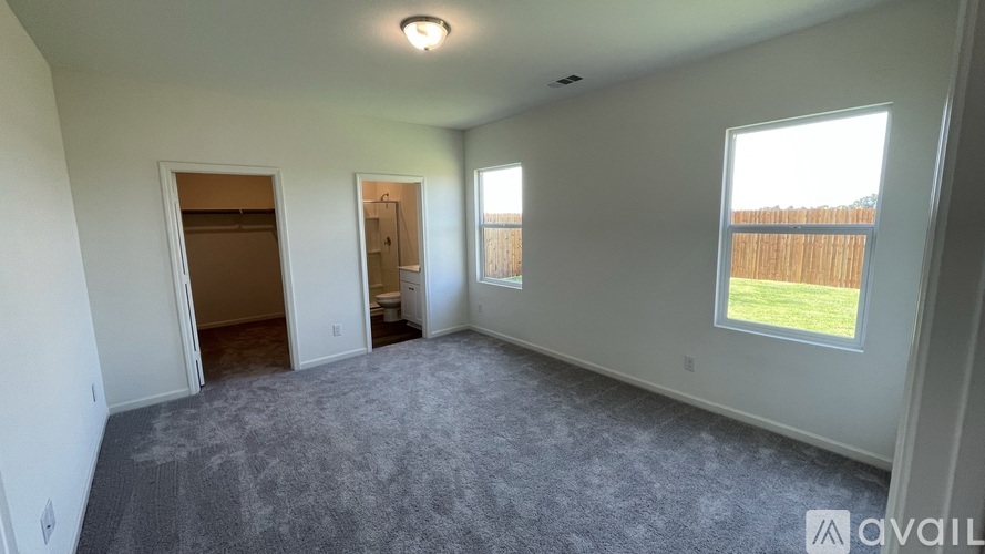 A spacious room with a grey carpet and a window overlooking a fence.
