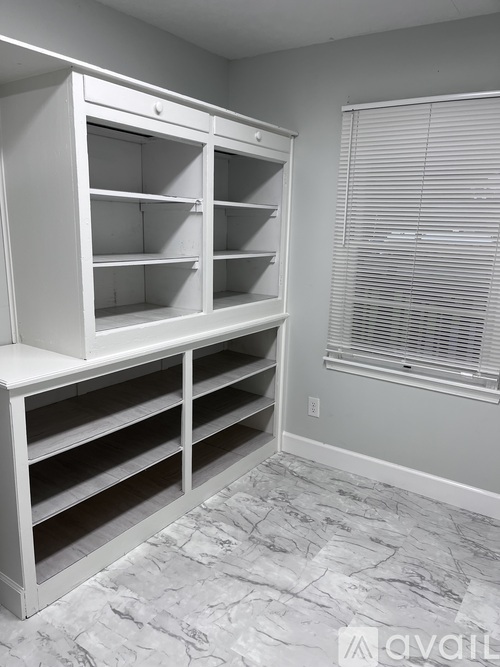 A white shelving unit in a room with a window covered by blinds.