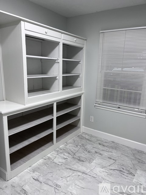 A white shelving unit in a room with a window covered by blinds.