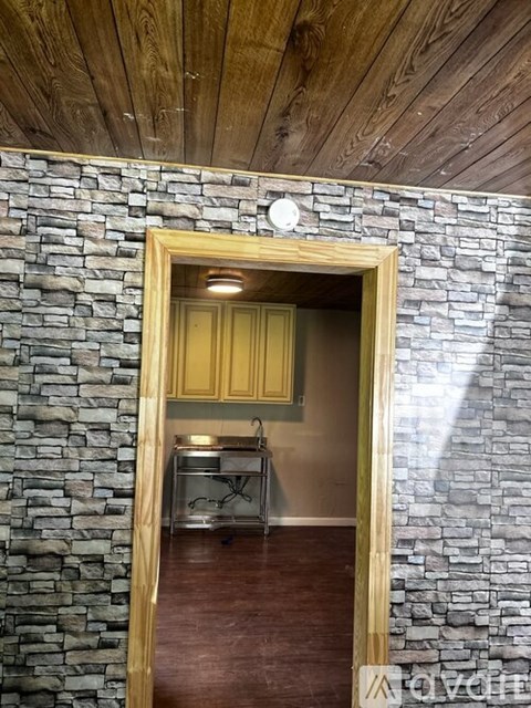 A stone wall with a wooden frame doorway leading to a kitchen.