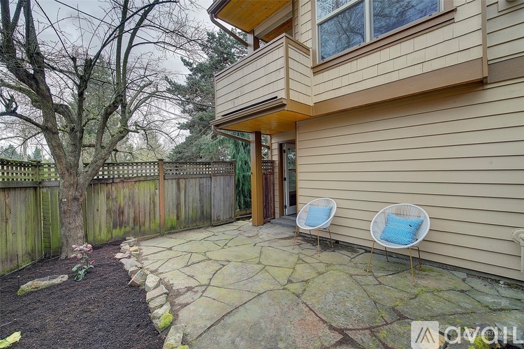 A patio with a stone walkway and two chairs with blue cushions.