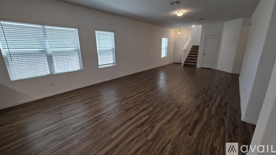 A spacious room with wooden flooring and a staircase in the background.