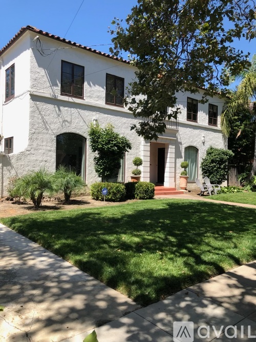 A white house with a green door and a tree in front.