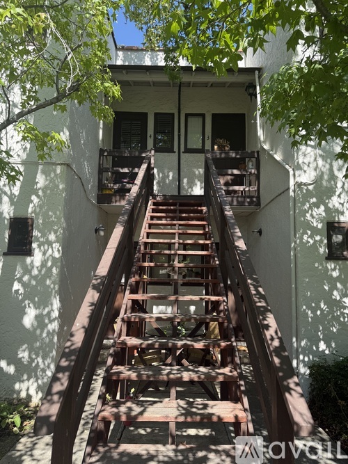 A wooden staircase leads up to a balcony on a white building.