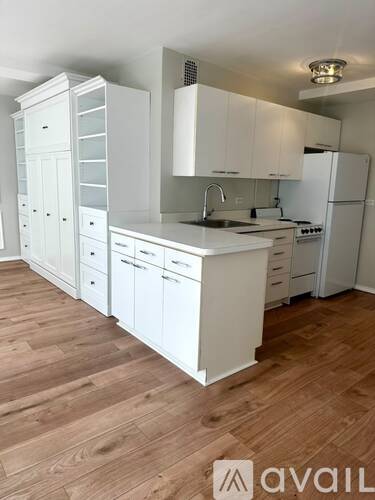 A kitchen with white cabinets and appliances on a wooden floor.