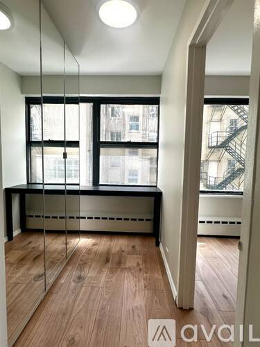 A room with wooden floors and a large window with a view of a building outside.