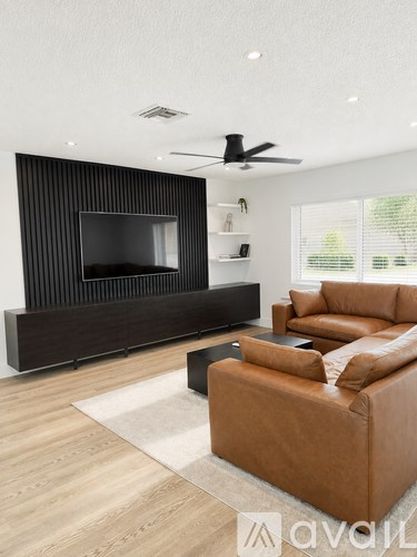 A living room with a brown leather couch and a flat screen TV mounted on a black wall.