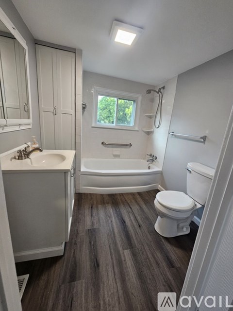 A white bathroom with a wooden floor and a window.