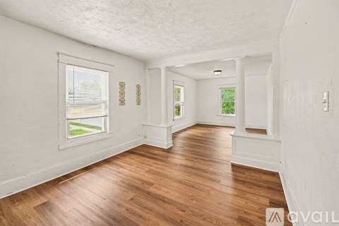 A room with wooden floors and white walls, with a window showing a green landscape.