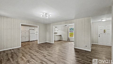 A room with wooden flooring and white walls, with a door open to another room.