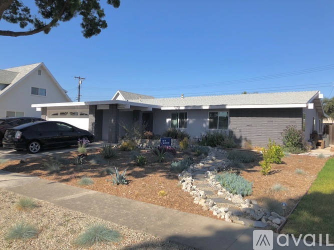 A house with a car parked in front and a garden with a variety of plants.