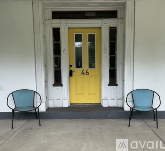 Two chairs are placed in front of a yellow door with the number 46 on it.