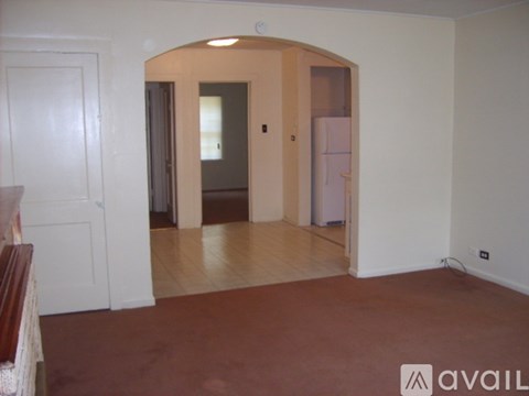 A room with a brown floor and white walls has a doorway leading to another room.