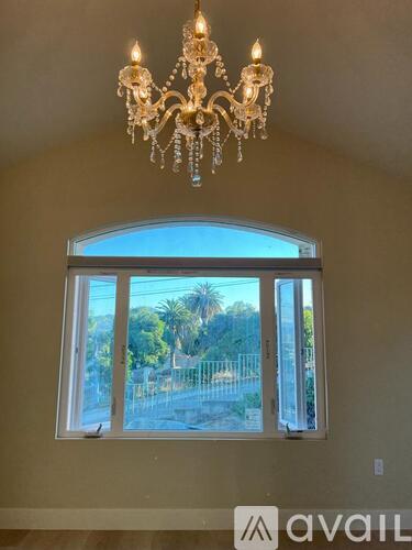 A chandelier hangs over a window with a view of a pool and trees.