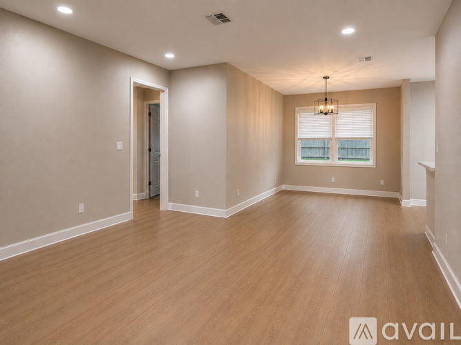 A spacious room with wooden flooring and a window with blinds.