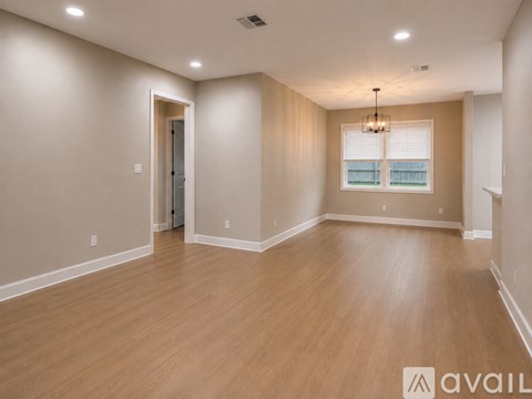 A spacious room with wooden flooring and a window with blinds.